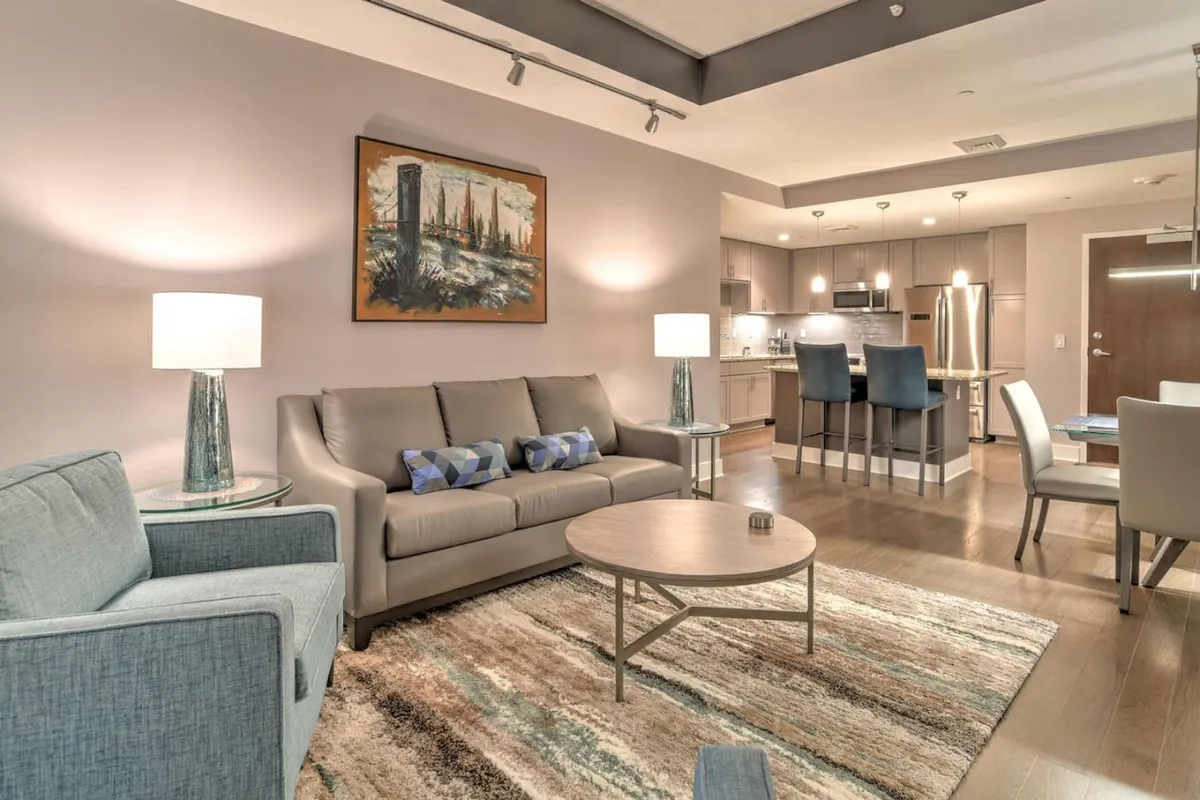 A modern living room with a plush sofa, coffee table, and vibrant artwork creates a welcoming environment ideal for small groups to relax or entertain. The lighting and ample seating suggest an inviting shared area for downtime, conversation, or planning the next adventure.