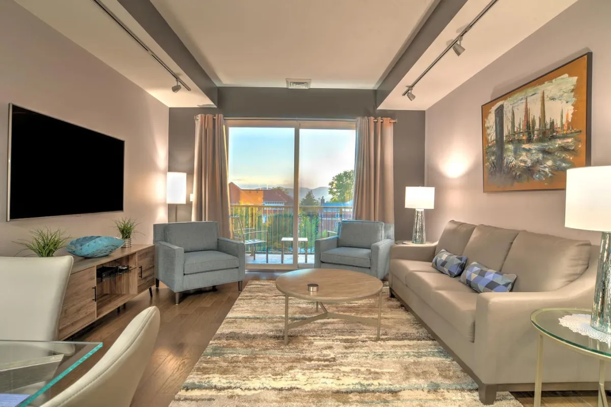 A spacious living room with a plush sofa, modern coffee table, striking artwork, and a large window that fills the room with natural light. The window offers sweeping views, while the furnishings exude comfort and contemporary style, perfect for social gatherings or quiet relaxation.