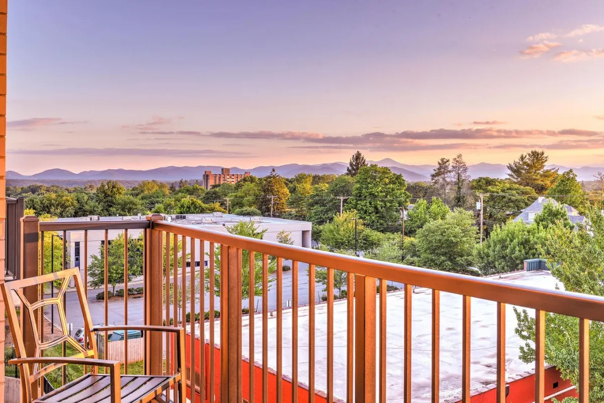 A tranquil shot of the balcony with lush greenery below, a clear mountain view in the distance, and a touch of sunset light illuminating the scene. The seating area beckons with the promise of relaxed mornings and peaceful evenings.