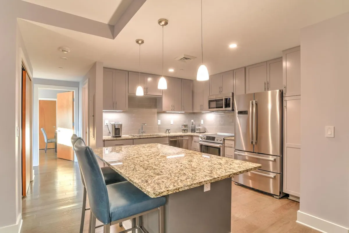 A modern, inviting kitchen scene highlighting sleek granite countertops, stainless steel appliances, and stylish pendant lights. The layout provides plenty of workspace, ideal for preparing meals or mixing craft cocktails, and evokes a sense of creativity and celebration.