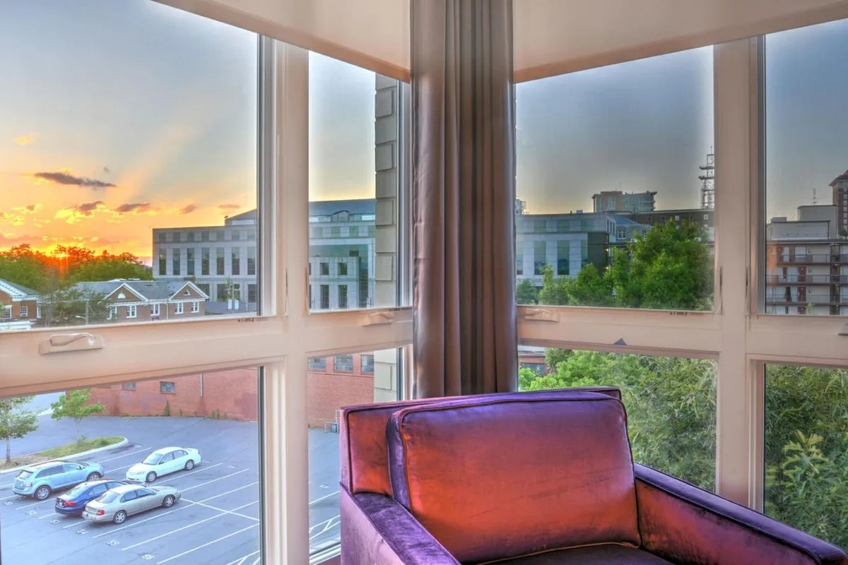 A serene balcony scene at golden hour, featuring a comfortable purple chair facing out over an urban landscape, with mountains visible in the background. The sky glows with sunset colors, inviting relaxation and contemplation. The setup encourages enjoying the views and the ambiance of the evening.