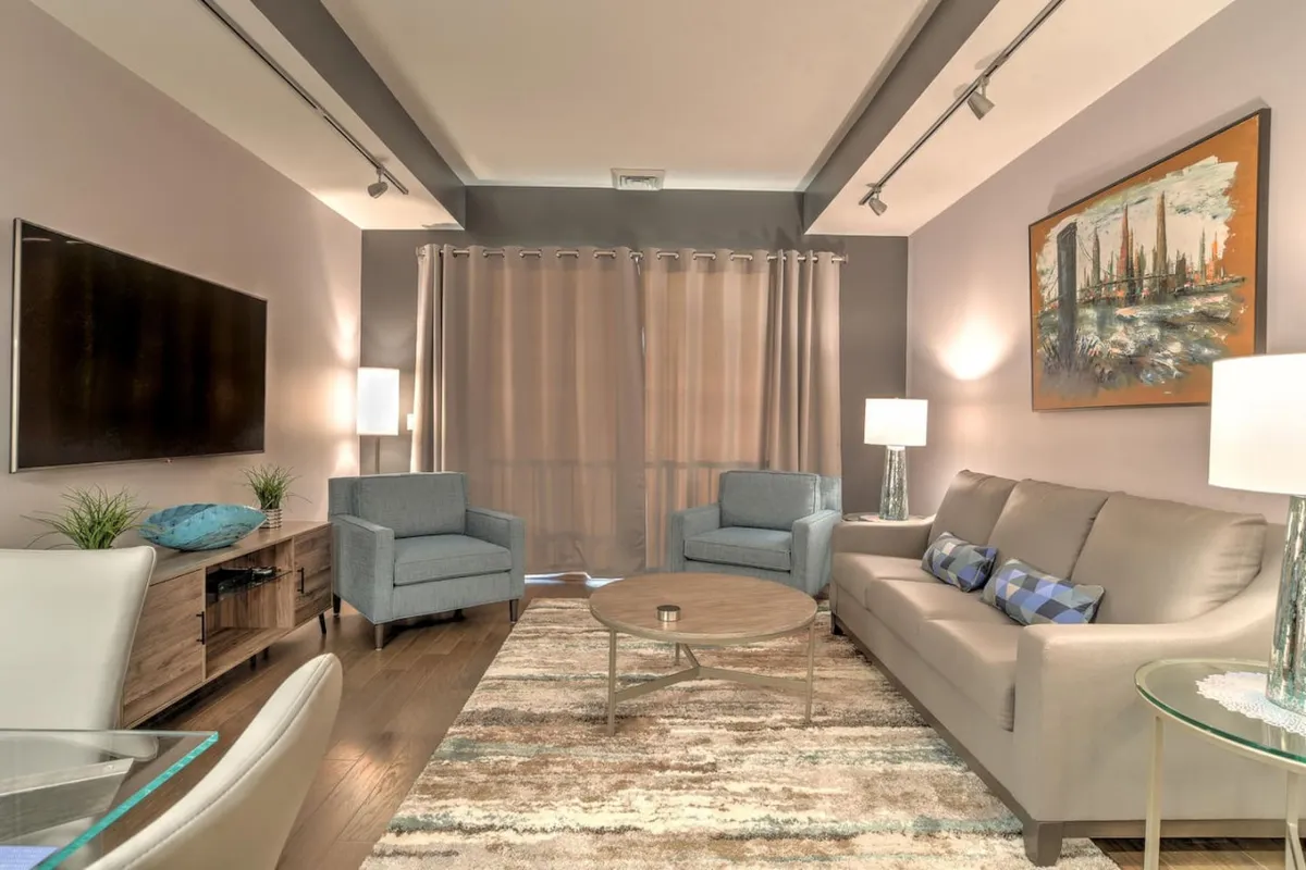 An inviting living area with a comfortable sofa, coffee table, wall-mounted TV, artwork, and curtains. The ambiance is cozy yet modern, suggesting a space equally suited for entertaining guests or enjoying a quiet evening in.