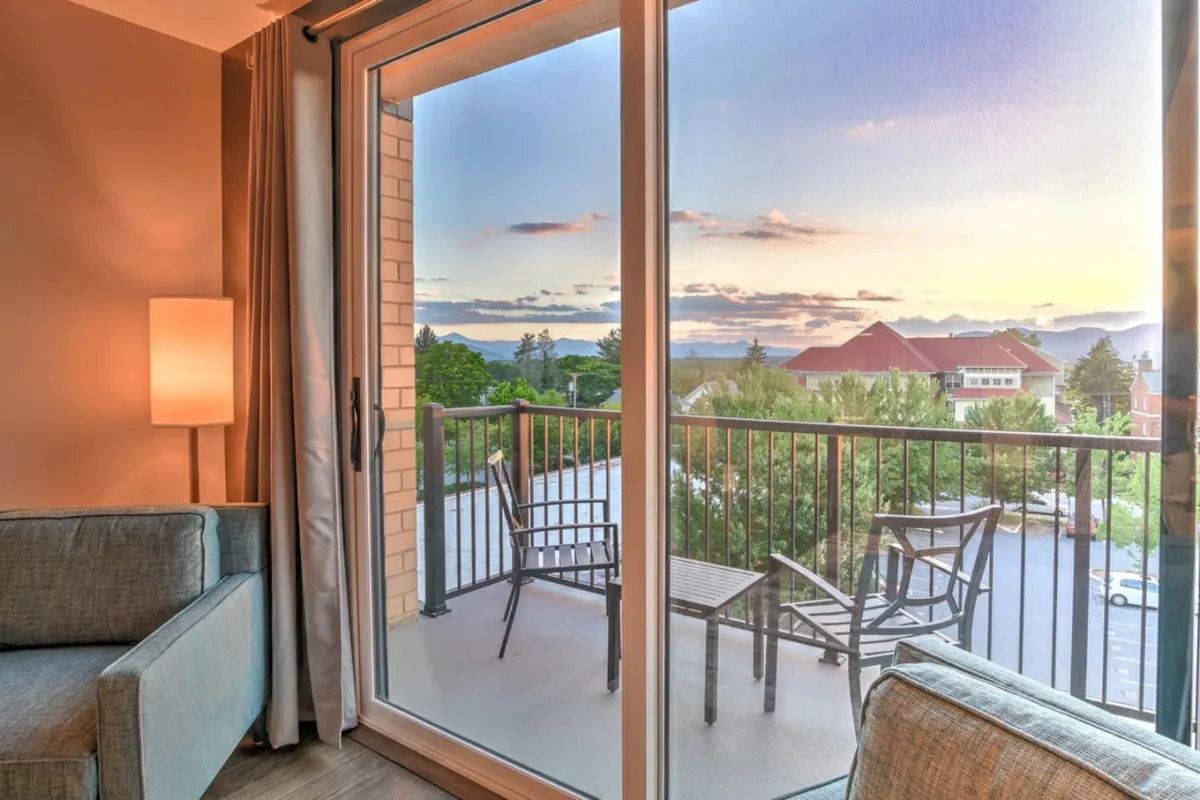An inviting interior scene showing comfortable seating positioned to enjoy expansive balcony views, softly illuminated by a lamp. The setup invites guests to unwind with a book or beverage while overlooking the landscape beyond.