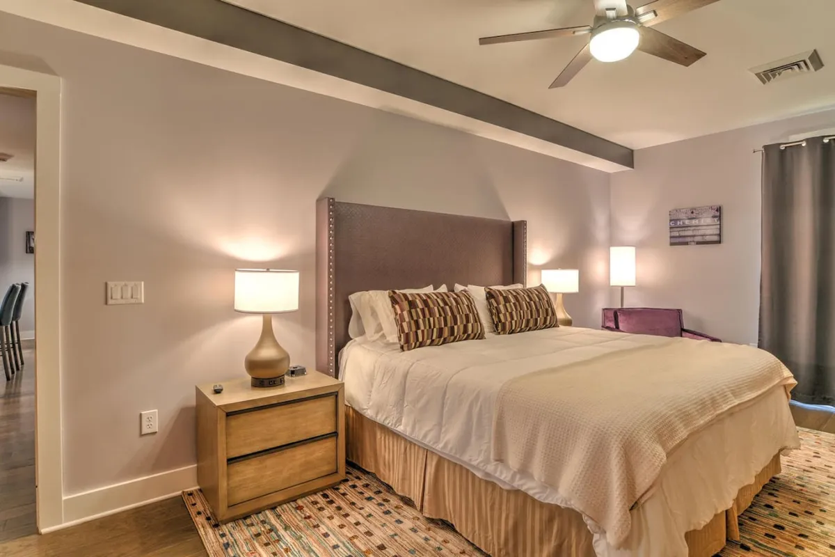 A calm and restful bedroom scene with a plush bed, nightstands topped with lamps, and a soft area rug. The space is softly illuminated, suggesting a serene ambiance ideal for relaxation and sleep.
