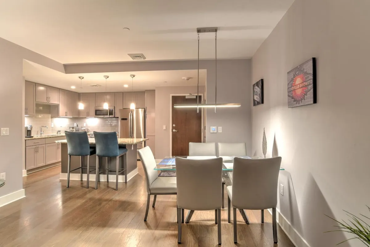 A contemporary dining area featuring a sleek dining table, a kitchen island, pendant lighting, and vibrant artwork on the walls. The layout is open, promoting easy flow between dining and kitchen spaces, and is ideal for both intimate dinners and larger social events.