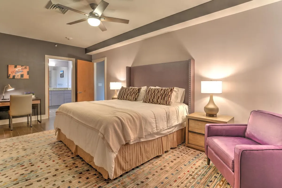 A cozy bedroom featuring a comfortable bed, a purple accent chair, and nightstands. The space feels inviting and functional, suitable for relaxation, reading, or quiet family moments. The room is well-lit and thoughtfully designed, enhancing comfort and rest for guests of all ages.